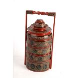 A painted and decorated tiffin carrier of five sections, with liner, bowl and saucer to the top,