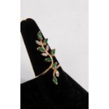 A modern diamond and emerald set ring modelled as a trail of leaves, to a 14k gold shank,