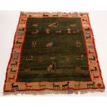 A Persian Gabbeh rug, central dark green field within a cream border lined in red, motifs of birds,