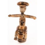 A carved and painted tribal figure modelled with arms outstretched and seated on a barrel,