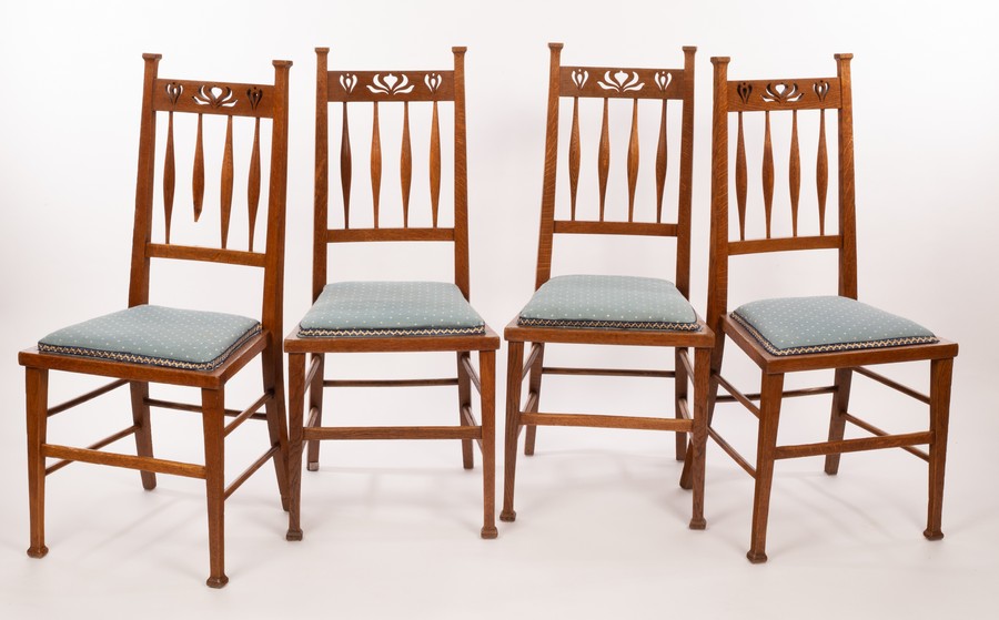 A set of four Art Nouveau oak dining chairs, with pierced crest rails and spindle backs,