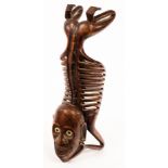 A tribal carving of a kneeling skeletal figure, the grinning face with ivory eyes,