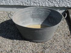 A galvanised bath with carry handles, 22.5in wide
