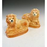 Pair of Staffordshire style reclining lions with orange glaze and gilt highlights, 24.5cm high