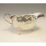 George V silver sauce boat with shaped rim, scroll handle and standing on three hoof feet,