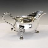 Edward VII silver sauce boat with shaped rim and scroll handle and standing on three shell feet,