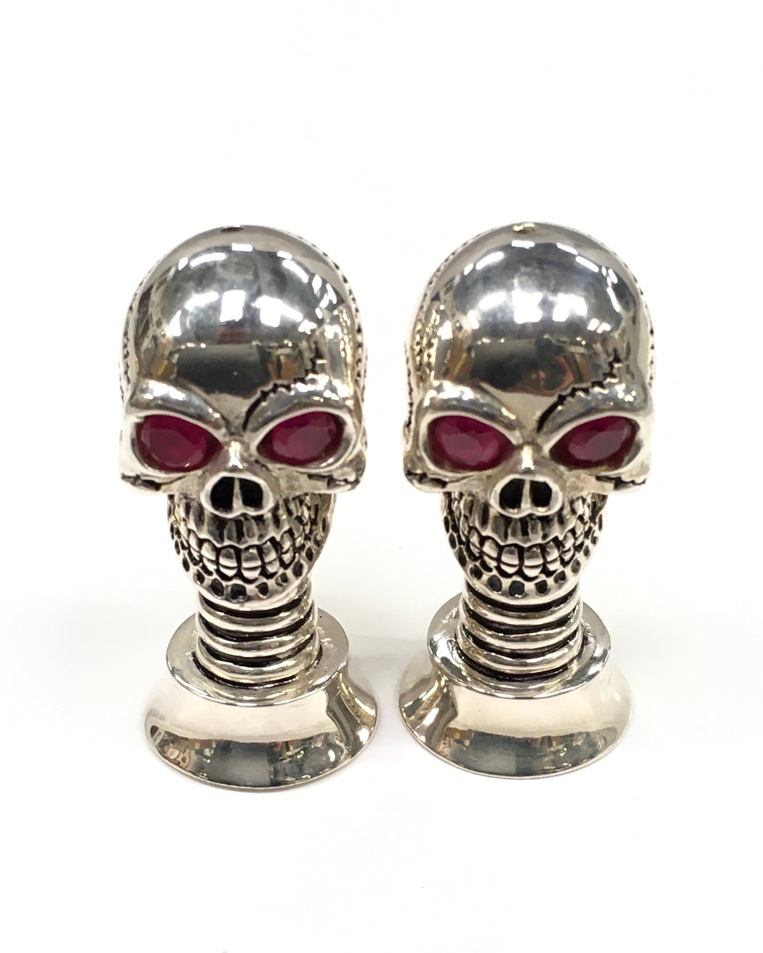 An unusual pair of silver plated scull shaped condiments with ruby eyes.