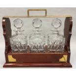 Brass and mahogany Tantalus with three crystal glass decanters to include the key.