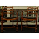 Pair of teak bar back carver armchairs with black leather seat pads.