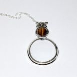 A silver magnifying glass owl shaped pendant with tigers eye cabochon.