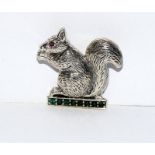 A silver squirrel brooch set on a emerald cultured stand with ruby eyes.