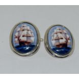 A pair of silver and enamel cuff links depicting ships at sail.