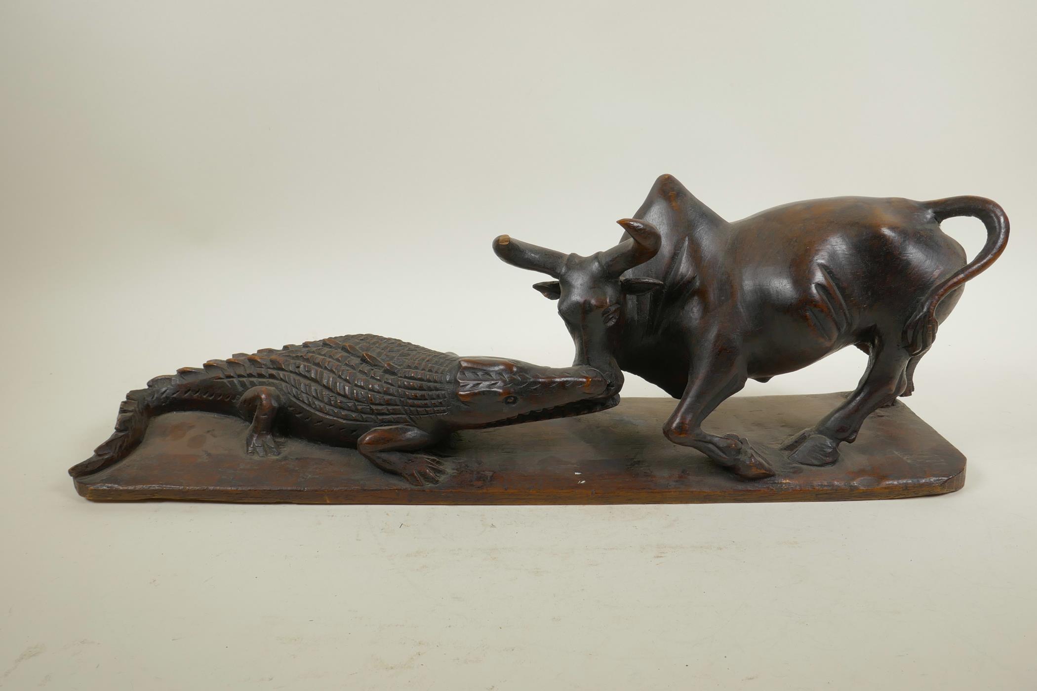 An African carved hardwood figure group decorated with a crocodile attacking a buffalo, 20½" long,