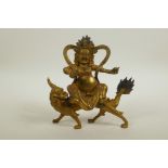 A Sino-Tibetan gilt bronze of a wrathful deity riding a mythical beast, 8" high