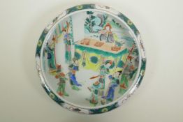 A Chinese famille verte porcelain dish with a rolled rim, decorated with figures in an interior