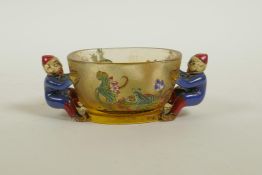 A Peking glass cup with two carved handles in the form of figures, the sides decorated in enamels