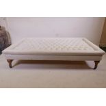 A large buttoned day bed/footstool upholstered in cream fabric, on brass castors, 65" x 38", 15"