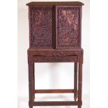 A Burmese hardwood cabinet on stand, with all over carving depicting Buddhistic scenes, the inset