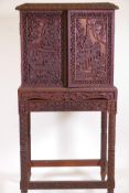 A Burmese hardwood cabinet on stand, with all over carving depicting Buddhistic scenes, the inset