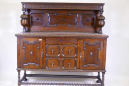 An early C20th oak court cupboard in two sections, with carved frieze and panelled back over a