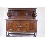 An early C20th oak court cupboard in two sections, with carved frieze and panelled back over a