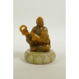 A Chinese amber soapstone carving of a Lohan with a temple lion on a carved green soapstone stand,