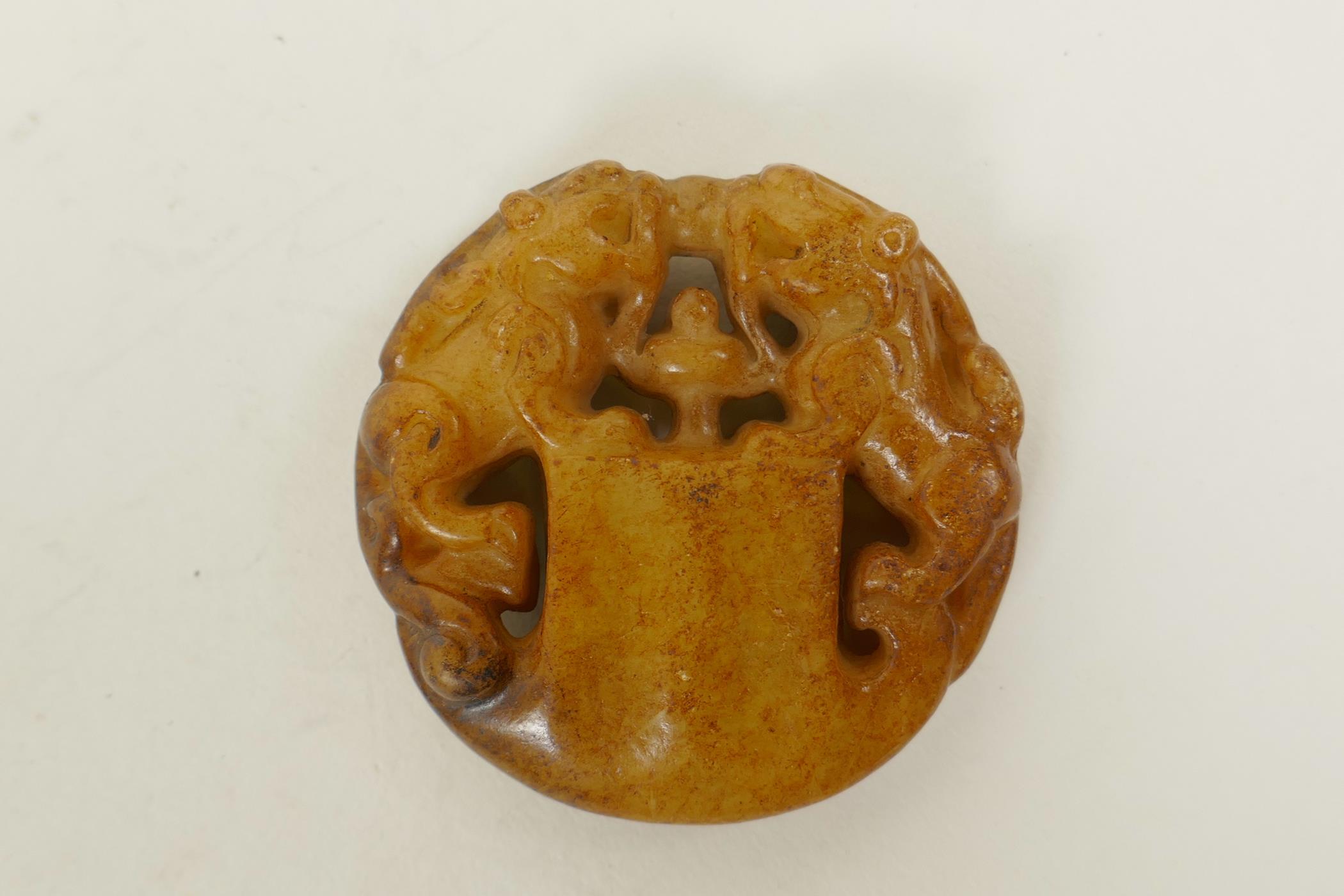 A Chinese russet hardstone pendant with carved twin kylin decoration, 2" diameter