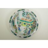A Chinese famille verte porcelain dish with a rolled rim, decorated with figures in an interior