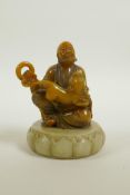 A Chinese amber soapstone carving of a Lohan with a temple lion on a carved green soapstone stand,