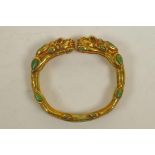 A gilt metal bangle in the form of two dragons, set with green and red lapis stones, 3" diameter