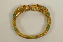 A gilt metal bangle in the form of two dragons, set with green and red lapis stones, 3" diameter