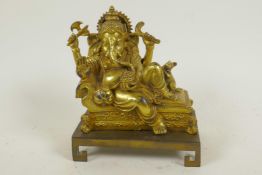 A gilt bronze figure of Lord Ganesh reclining on a couch, 5" long, on a key pattern plinth