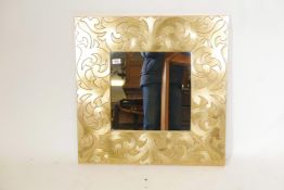 A moulded gilt mirror with raised scrolling decoration, 27" x 27"