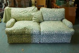 A two seater sofa bed with cream and green bamboo leaf pattern upholstery