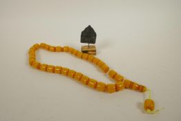 A string of Tibetan faux butterscotch amber mala beads, together with a Tibetan mounted metal