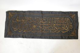A textile wall hanging embroidered with Islamic calligraphy, in gilt metal wire, 63" x 24"