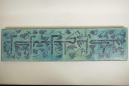 A Persian turquoise glazed four tile plaque decorated with an Eastern inscription, 8" x 31½"