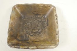 A Chinese white metal square section dish embossed with dragons and calligraphy, 3" square