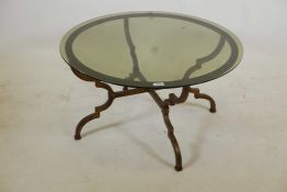 A gilded steel framed occasional table with shaped supports, cross stretcher and tinted glass top,