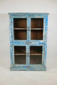 An Indian hardwood cabinet with four glazed doors and distressed paintwork, raised on a shaped