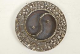 A Chinese white metal roundel/scroll weight decorated with the Yin Yang symbol, 3¼" diameter