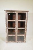 An Indian hardwood two door display cabinet with distressed paintwork, raised on stile supports, 35"
