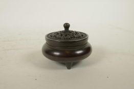 A Chinese bronze censer with a pierced cover and tripod supports, decorated with bats to cover and