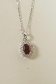 An 18ct white gold pendant necklace set with a garnet encircled by diamonds