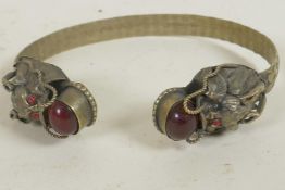 A Chinese white metal bangle, the terminals made as dragons' heads set with semi-precious stones,