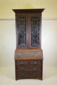 A C19th oak Arts and Crafts bureau bookcase, with stained glass doors, carved green-man details, the