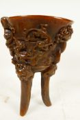 A Chinese faux horn libation cup on three legs, embossed with mythical beasts