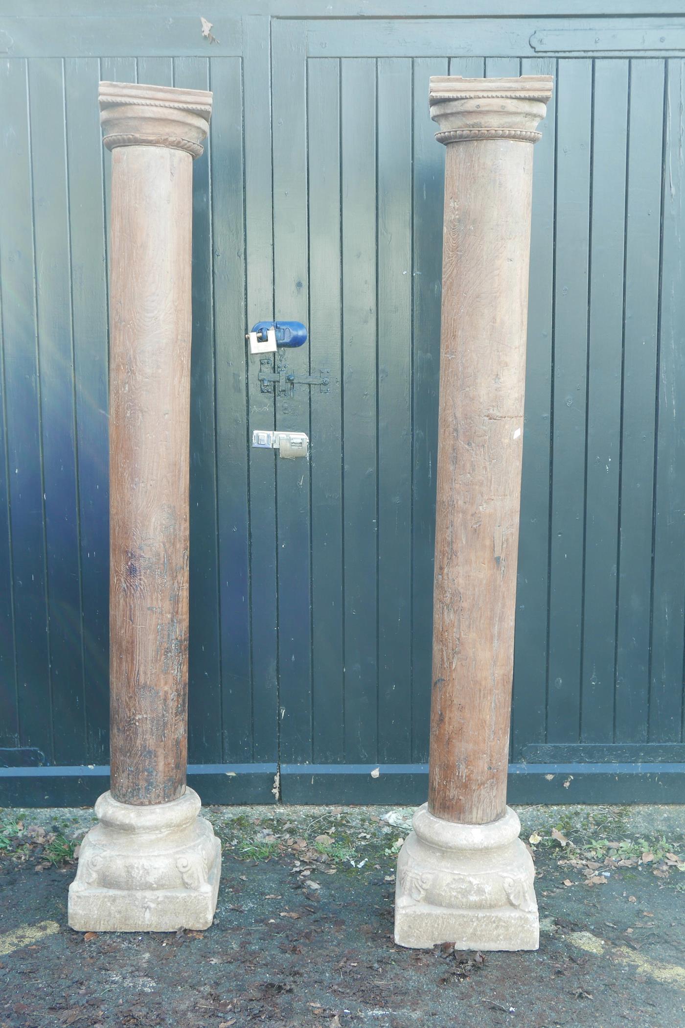 Architectural salvage: A pair of Indian teak columns with carved capitals, mounted on carved stone