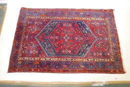 A Persian red ground wool carpet with a centralised medallion design on a blue border, 52" x 80"