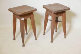 A pair of early C20th oak industrial bench stools, raised on tapering supports, one lacking cross